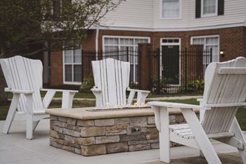 Three white chairs are arranged around a stone fire pit.